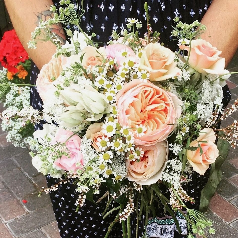 Bride holding a peach and blush garden-style bridal bouquet with roses, chamomile, and airy wildflower accents by A Secret Garden Vail Colorado