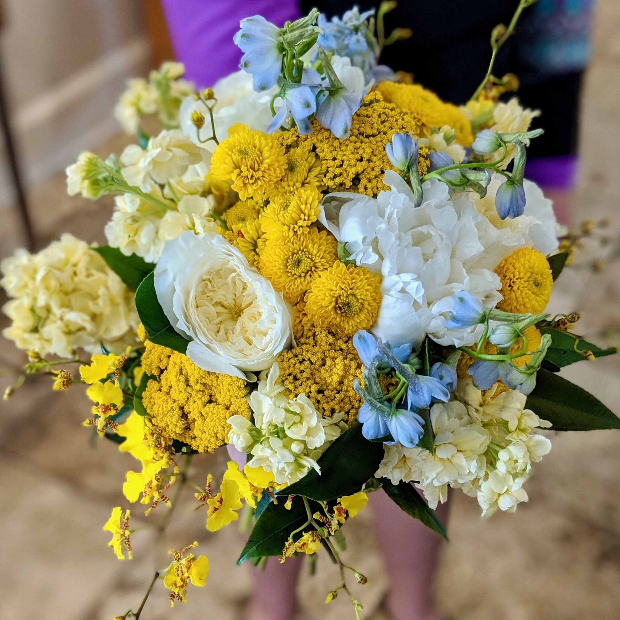 Bride holding a yellow and white garden-style bridal bouquet with roses, ranunculus, delphinium, and seasonal blooms by A Secret Garden Vail Colorado